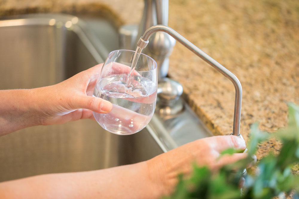 woman filling glass of water from reverse osmosis faucet